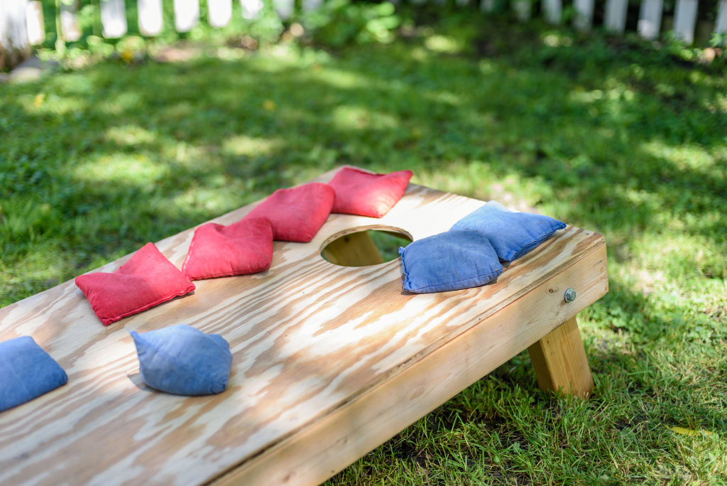 Wooden cornhole board with red and blue bean bags on green grass